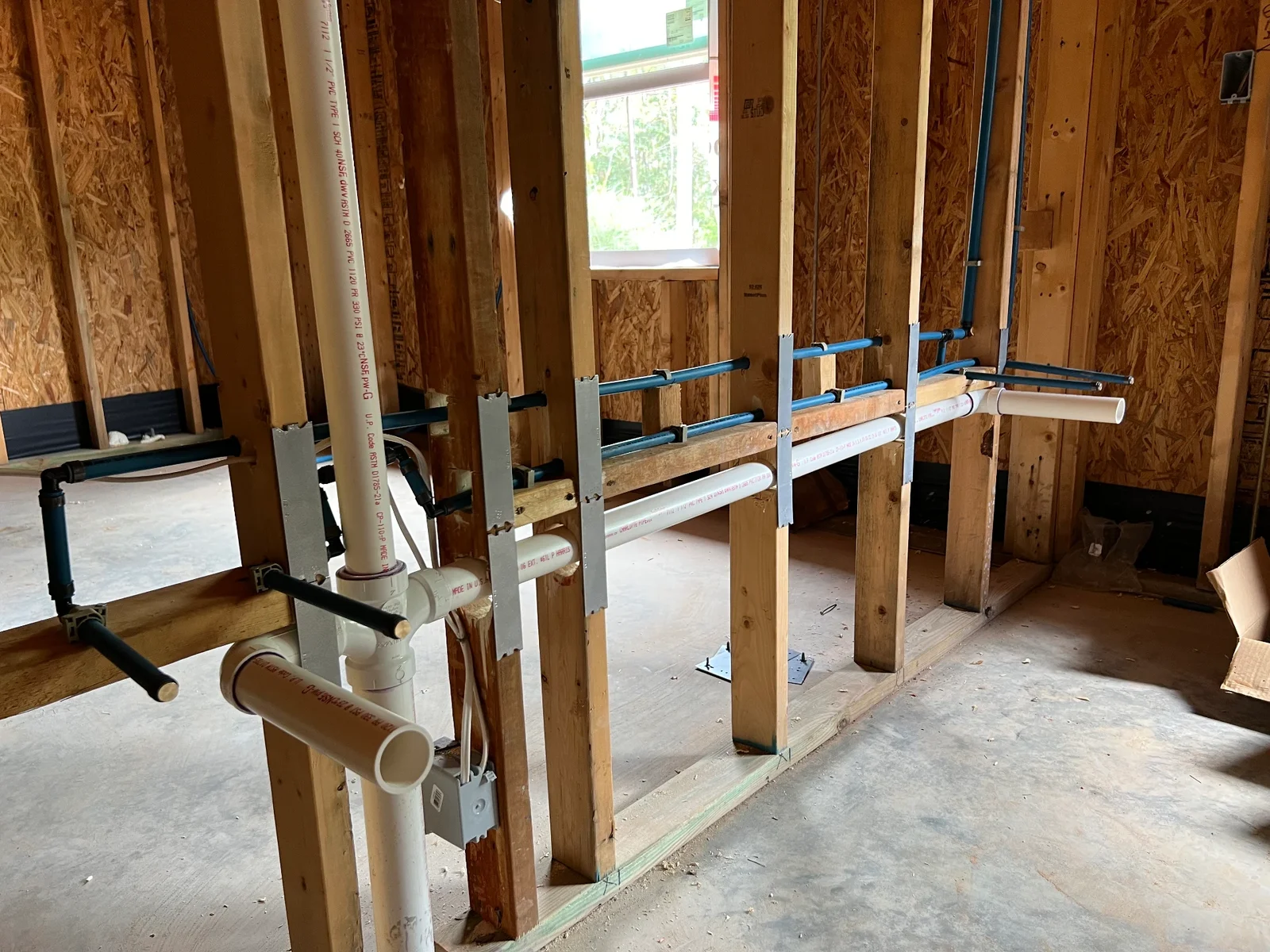 Bathroom plumbing rough-in with PEX supply lines and PVC drain piping between framed walls of a new home