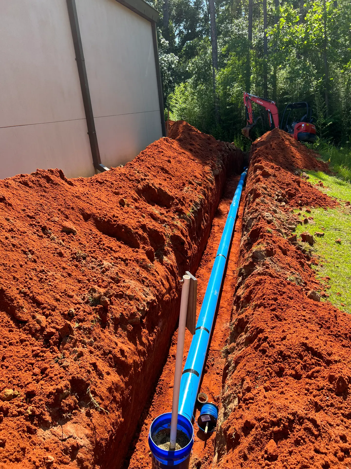 Long open trench with a new blue water service line run alongside a building